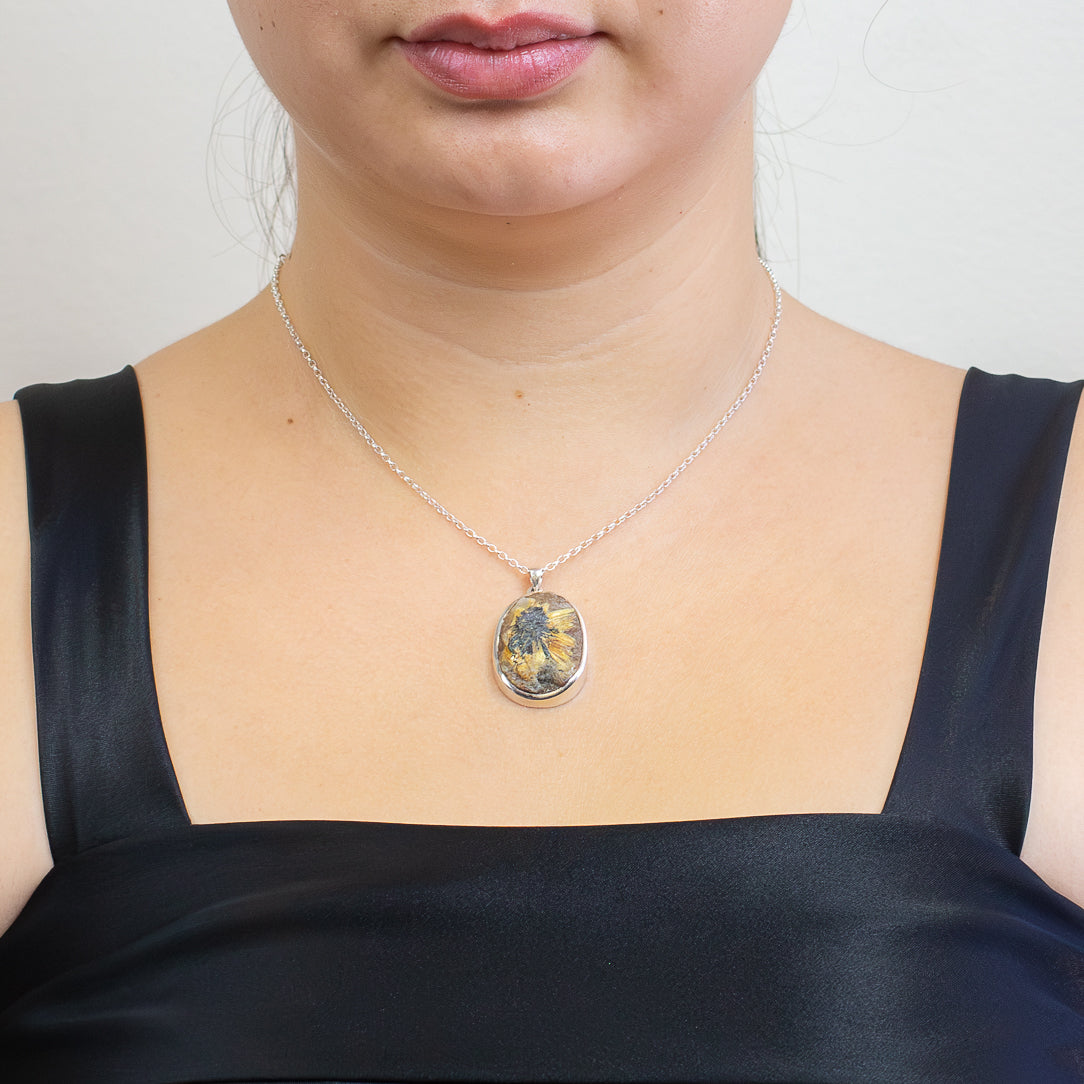 Raw rutilated quartz pendant with golden rutile bursts and dark hematite core, set in sterling silver on a chain.