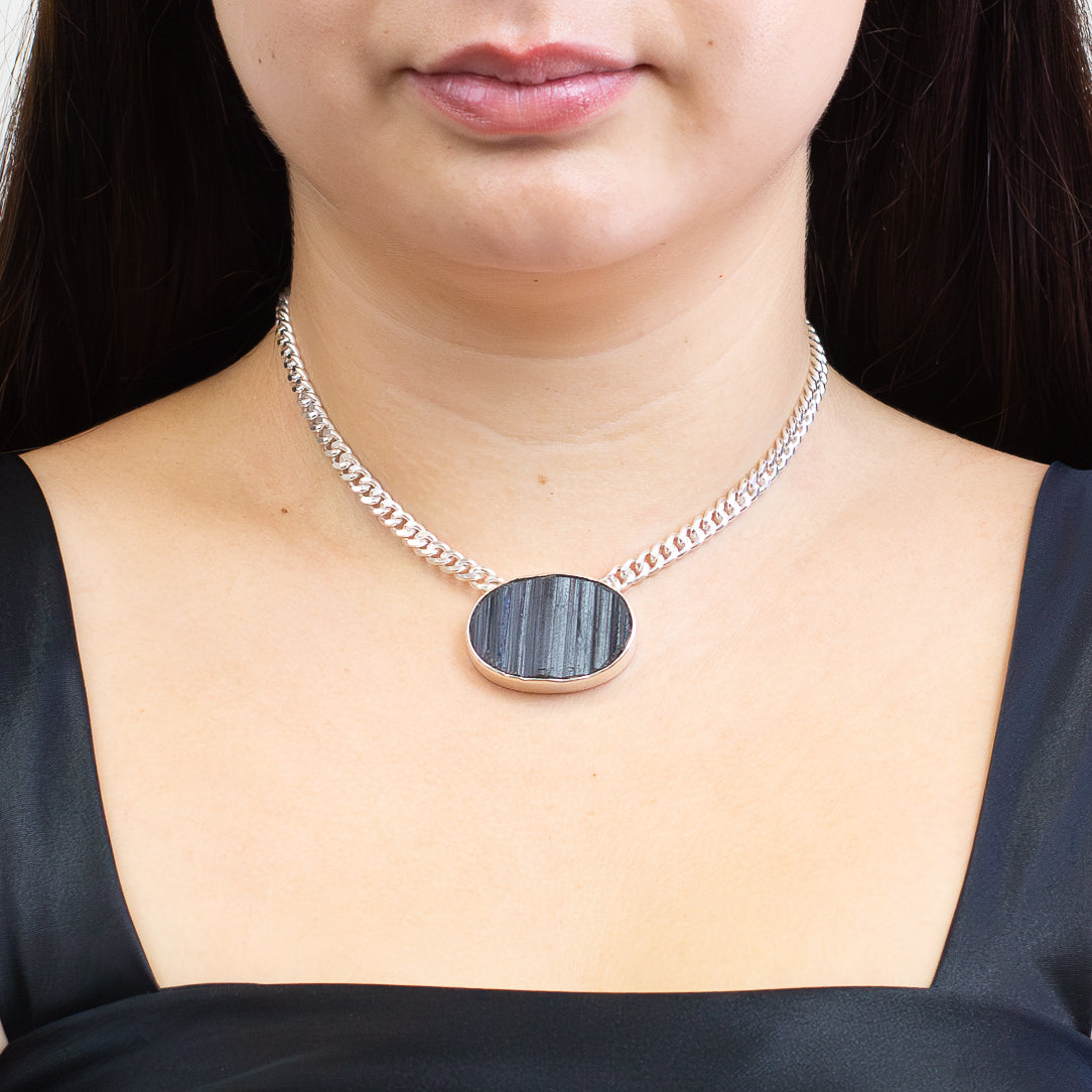 Raw oval black tourmaline pendant with natural vertical striations set in sterling silver with attached silver chain on model. | MADE IN EARTH