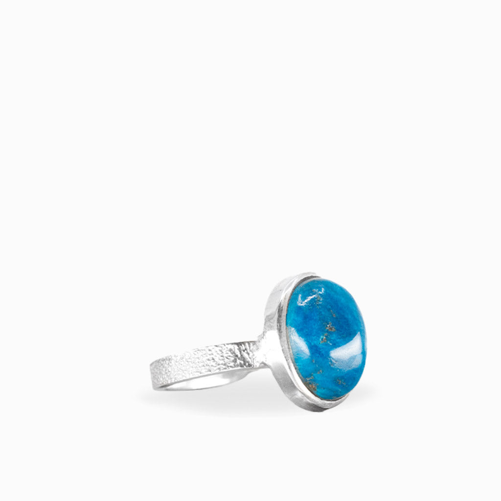 Oval Cavansite ring with vibrant ocean-blue cabochon, natural mineral inclusions, polished sterling silver bezel, and textured band.