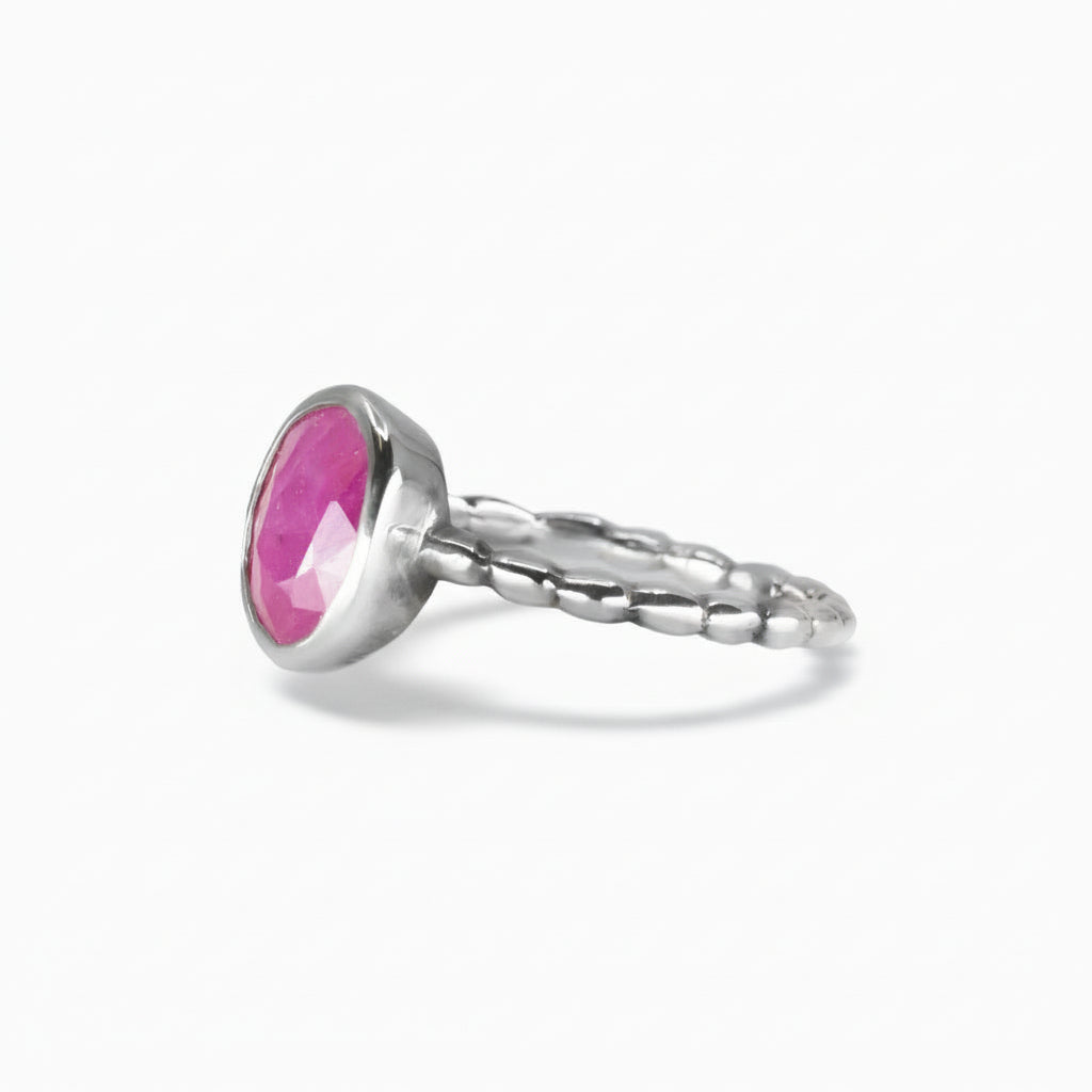 Faceted oval Ruby ring with vivid pink-crimson tones set in a polished sterling silver textured band on a white background. | MADE IN EARTH