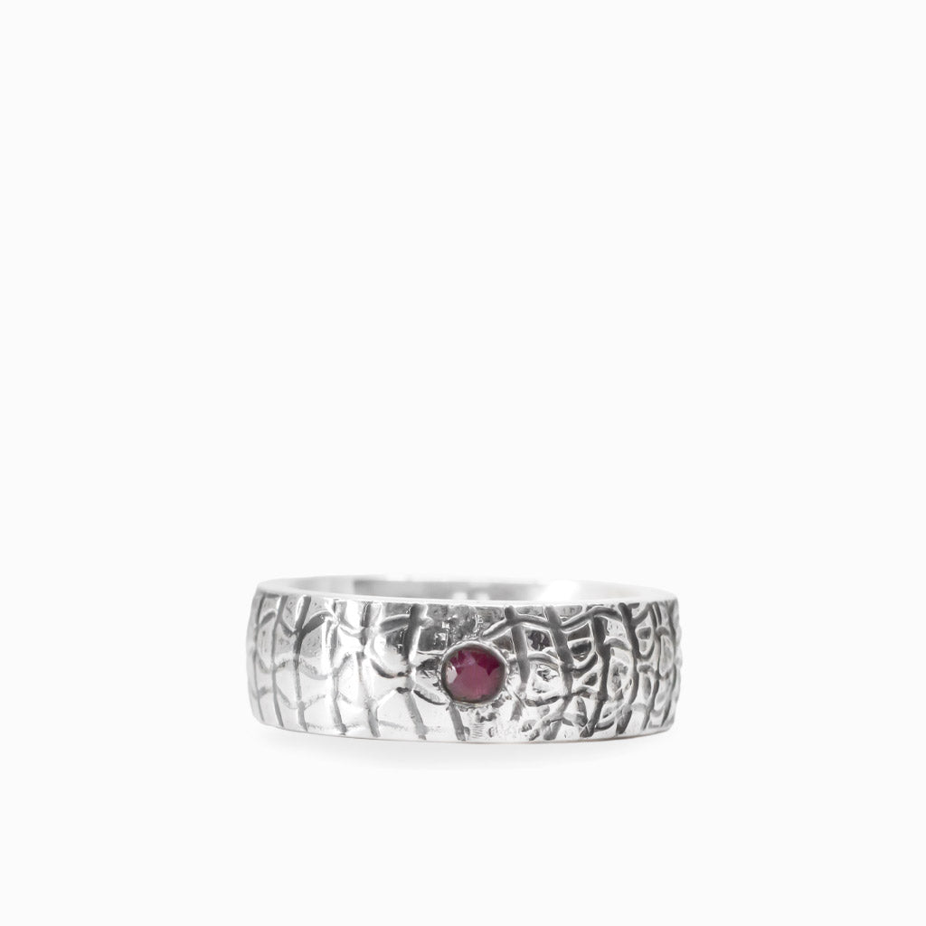 Small round red Ruby gemstone set into a wide textured 925 sterling silver band ring.