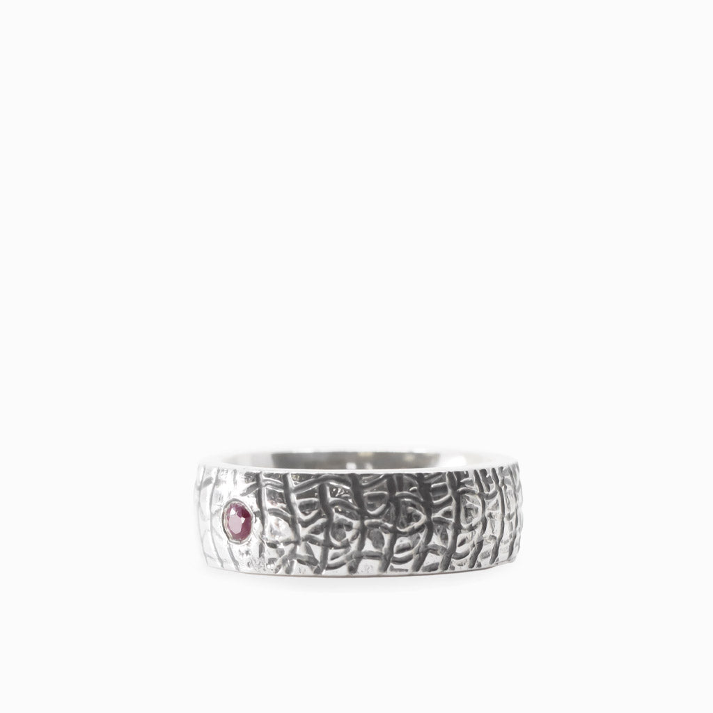 Small round red Ruby gemstone set into a wide textured 925 sterling silver band ring.