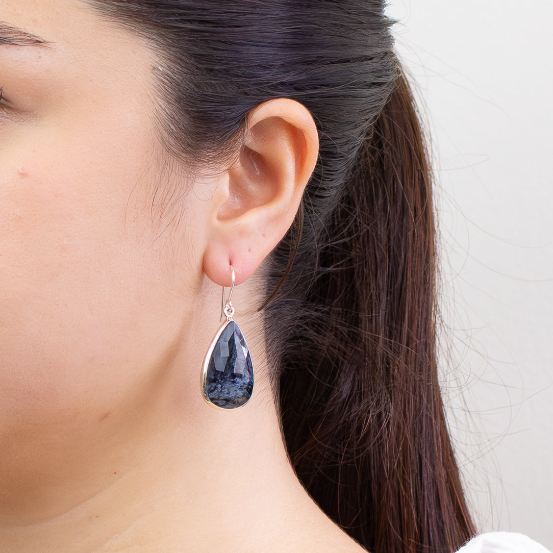 Faceted Pietersite teardrop earrings in sterling silver with swirling navy and gold patterns on model. | MADE IN EARTH