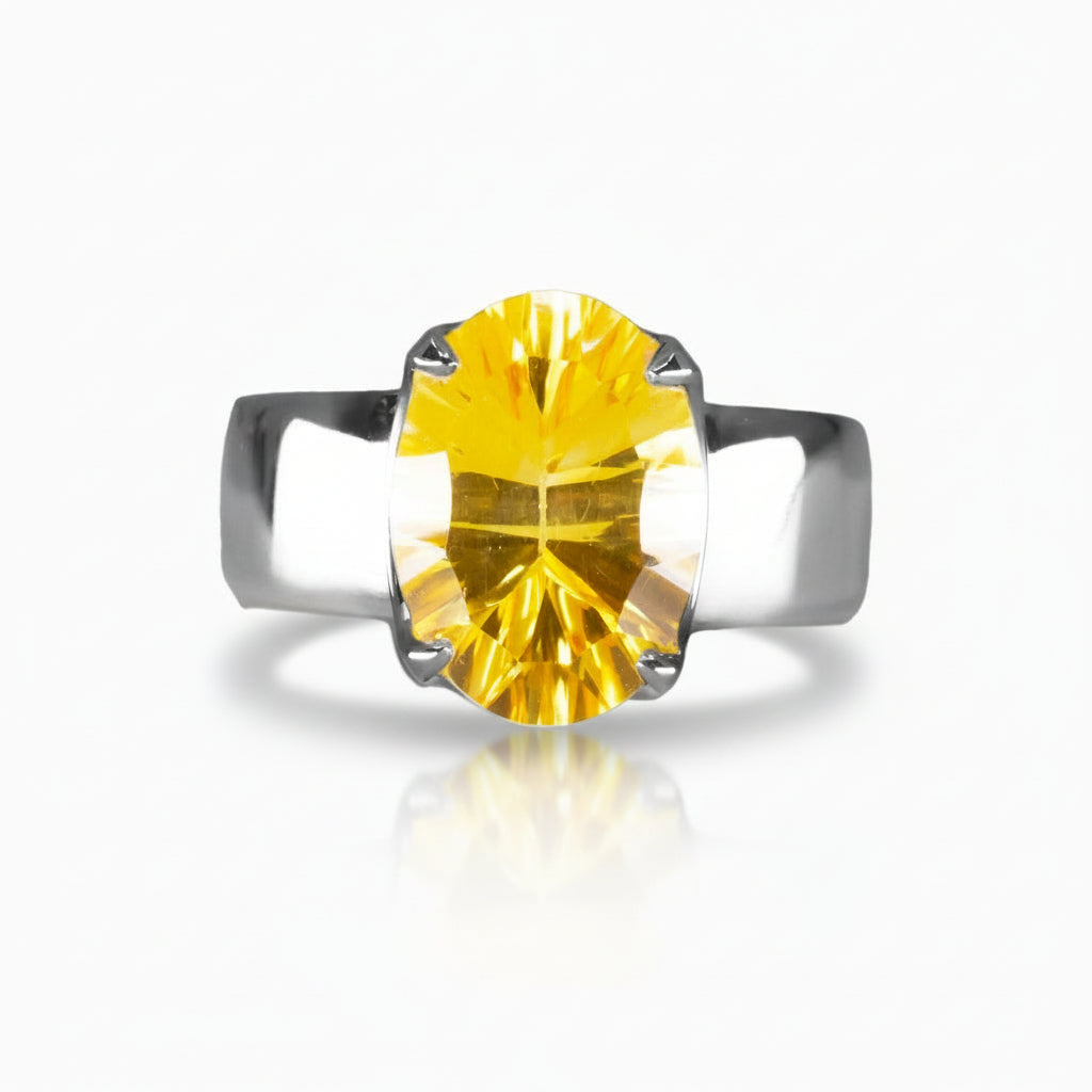 Faceted oval yellow Citrine ring set in a sterling silver prong setting with a wide silver band, photographed on a white background