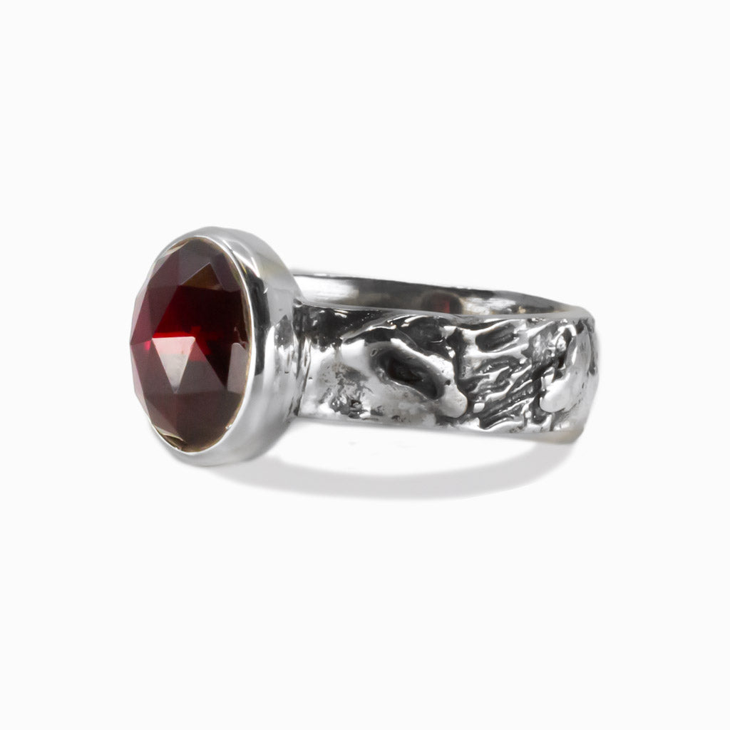 Garnet gemstone ring showing faceted oval stone set in textured silver band. | MADE IN EARTH