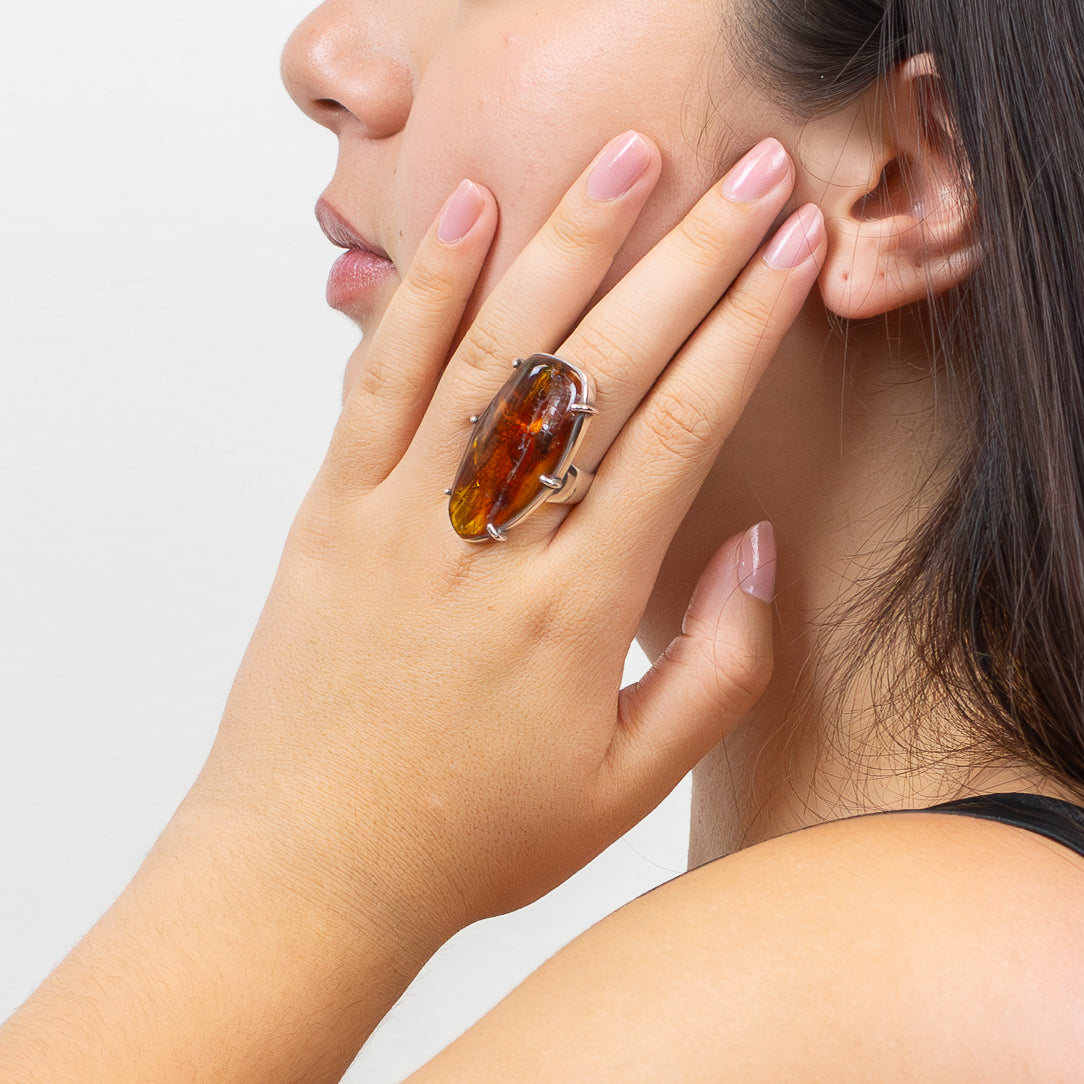 model wearing Organic-shaped Amber ring with warm golden-orange tones and natural inclusions set in a sterling silver prong setting on a white background. | MADE IN EARTH USA