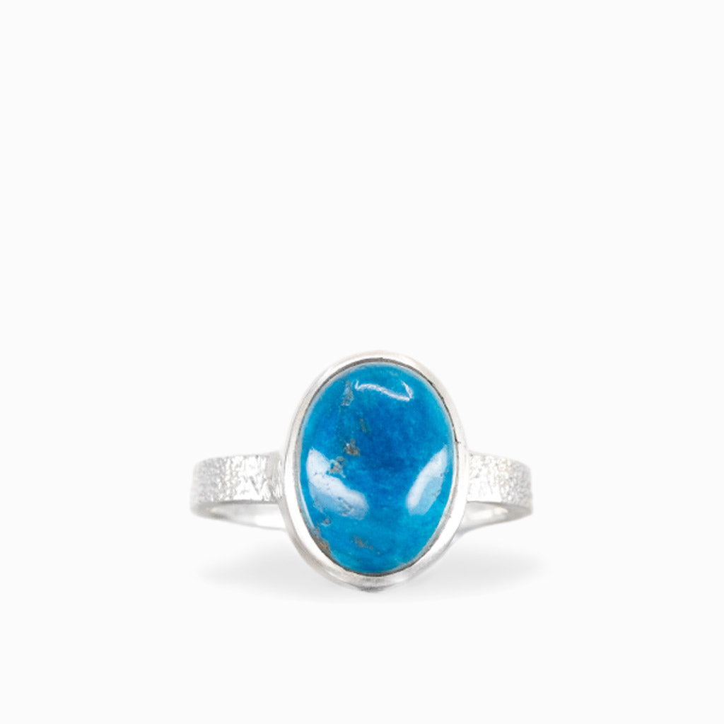 Oval Cavansite ring with vibrant ocean-blue cabochon, natural mineral inclusions, polished sterling silver bezel, and textured band.
