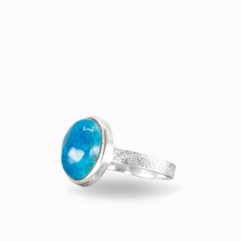 Oval Cavansite ring with vibrant ocean-blue cabochon, natural mineral inclusions, polished sterling silver bezel, and textured band.