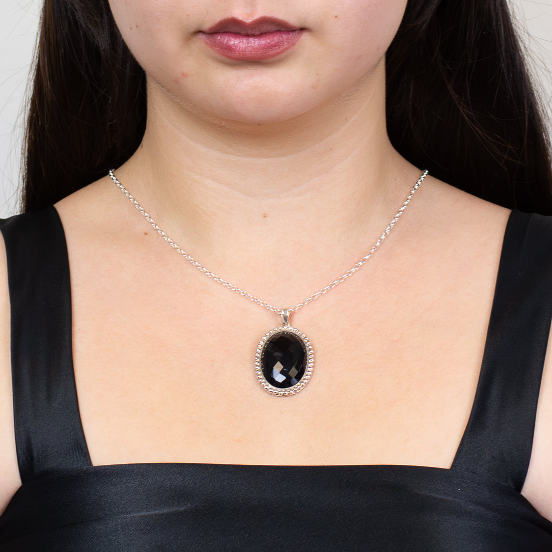 Faceted oval black onyx pendant set in sterling silver on chain  on model

