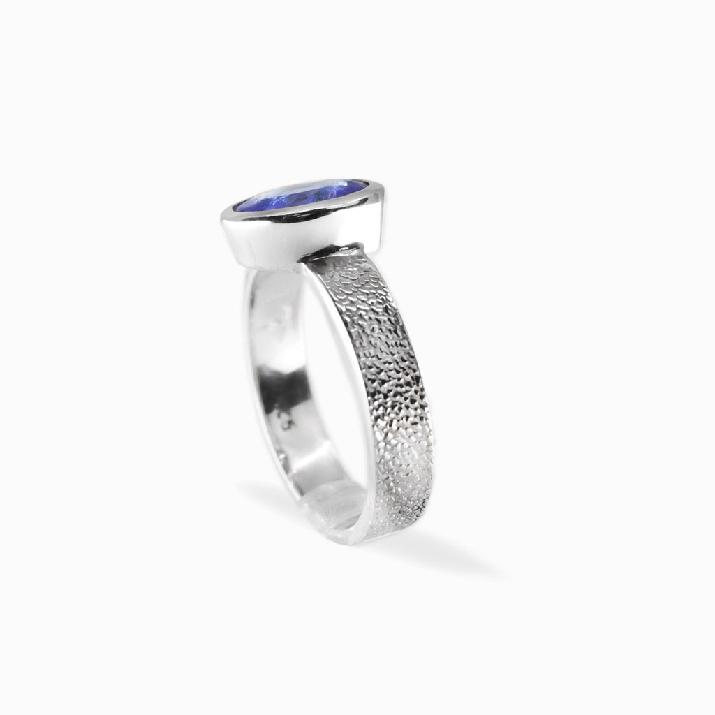 Oval faceted violet-blue Tanzanite ring in polished 925 sterling silver bezel setting with a broad textured silver band.