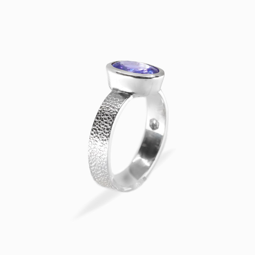 Oval faceted violet-blue Tanzanite ring in polished 925 sterling silver bezel setting with a broad textured silver band.